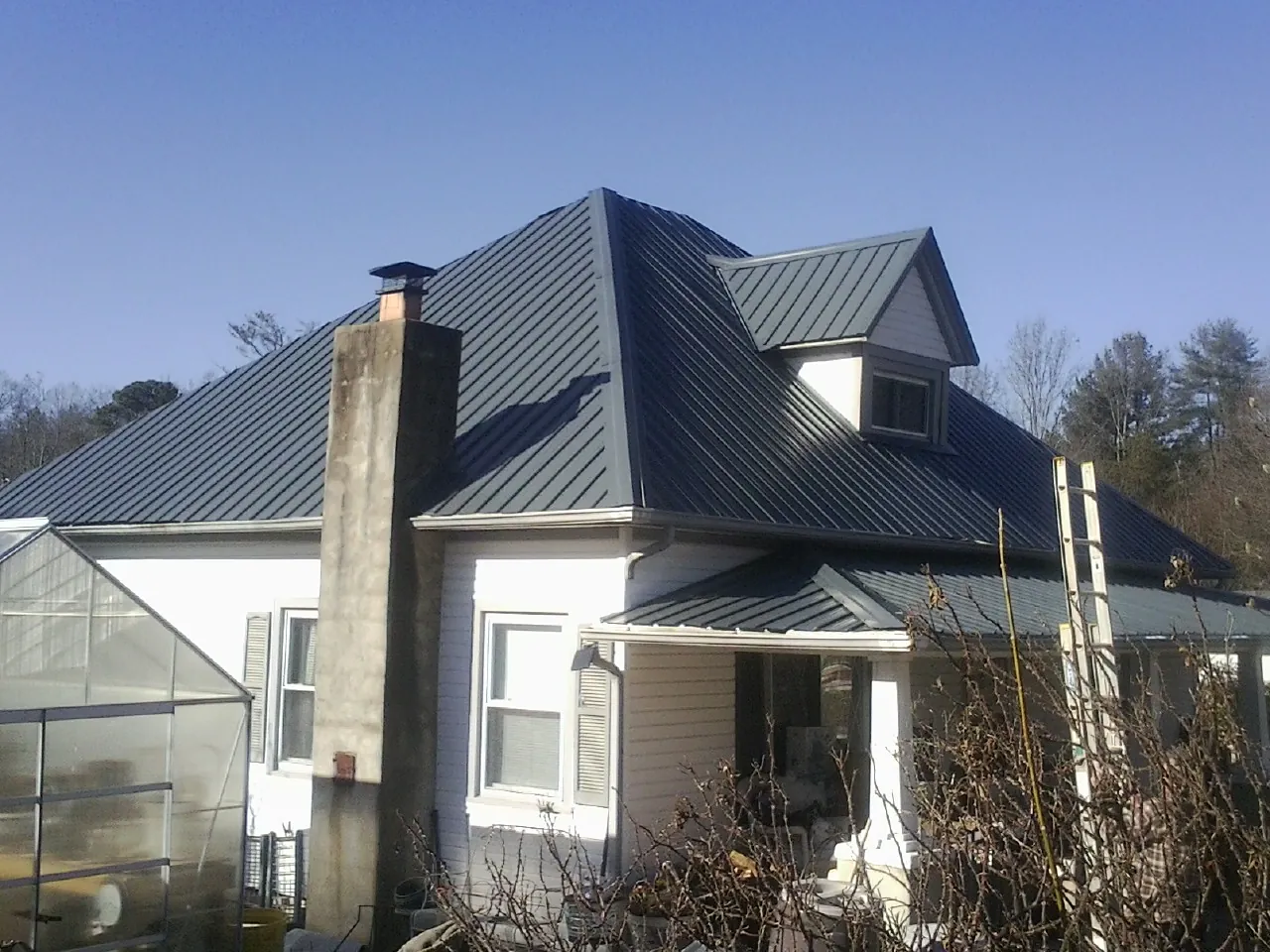 Dark blue standing seam metal roof on a white farmhouse with dormer — Slate & Tile Roof Repair by Roofing Brothers in Carbon Hill