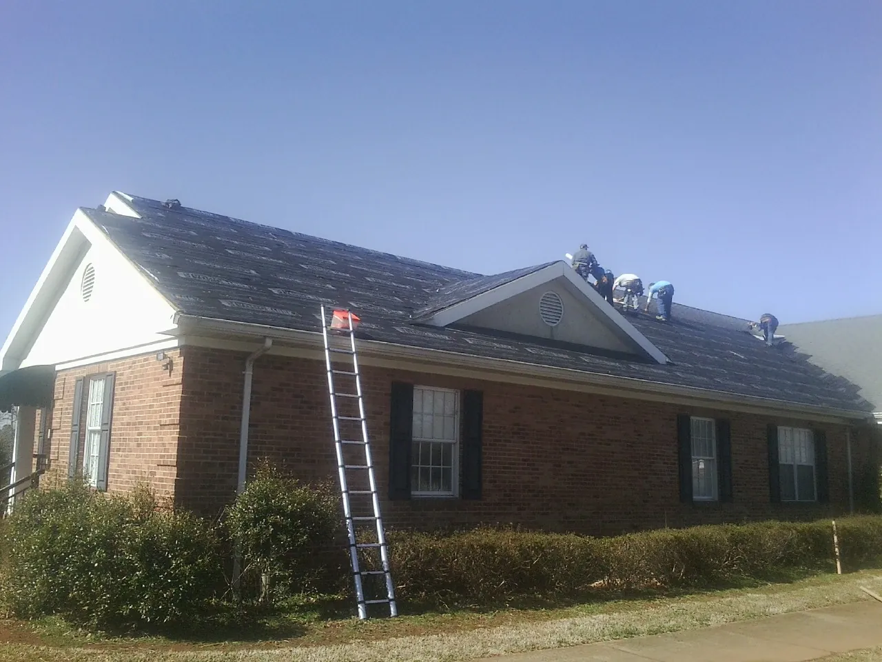 Crew tearing shingles off a brick ranch roof with a ladder set — Metal Roof Repair work by our crew in Carbon Hill