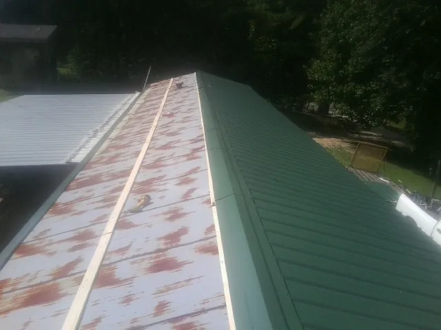 Old rusted panels beside newly installed green metal roofing — Wind Damage Roof Repair by Roofing Brothers in Carbon Hill