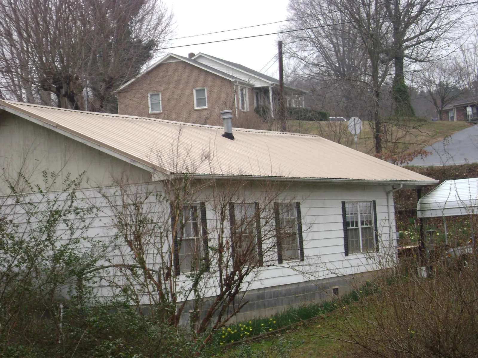 Tan metal roof on a white sided house set into a hillside — Commercial Roofing by Roofing Brothers in Carbon Hill